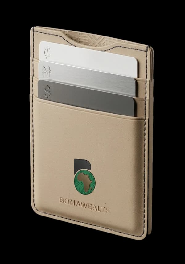 A sand-coloured leather BomaWealth wallet holding three cards engraved with the cedi, naira and dollar signs